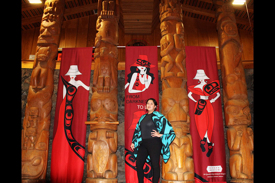 Justina Moore, Ksim Gisk’aast from Wilps Niisyuus, stands in front of the event banners at Gitlaxt’aamiks Recreation Centre. Justina is wearing drop killer whale crest earrings made of acrylic with abalone drop posts designed by Jaimie Davis. The banner designs were created by Tsimshian and Nisga’a artist Shawna Kiesman. (Michael Bramadat-Willcock/Terrace Standard)