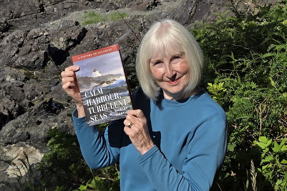 Shirley Martin standing in front of the Amphitrite Point Lighthouse with her soon-to-be released book.