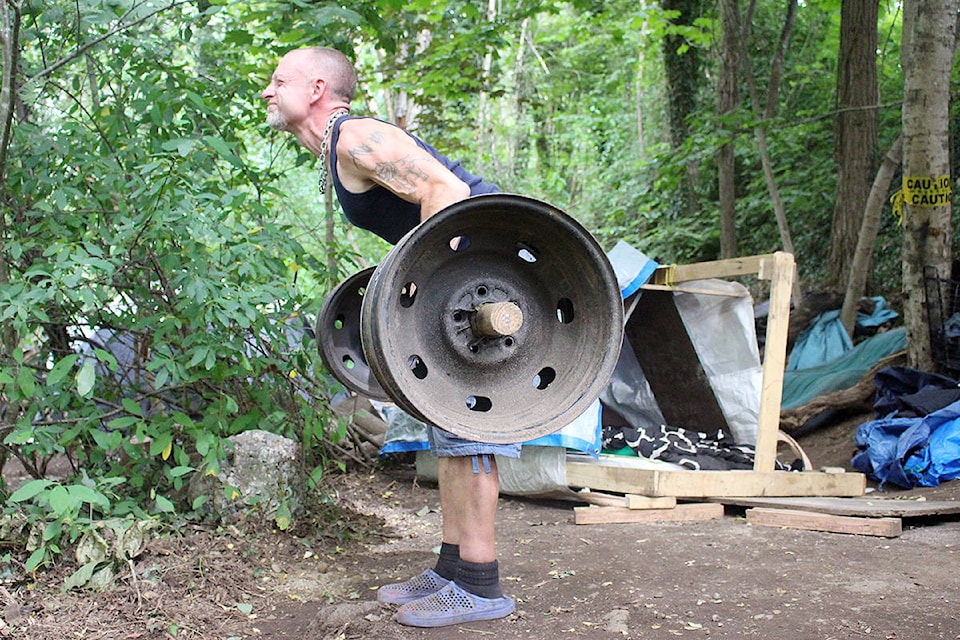 Photo: Lauren Collins Shane Knight, who lives in the tent city just off of King George Boulevard in a forested area near Bridgeview, demonstrates some of the exercises he can with the workout equipment he built in the camp from scrap materials.