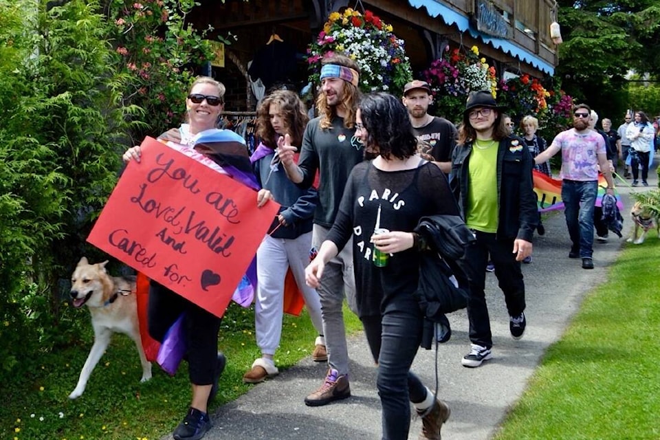 Toni Buston walks up Peninsula Road and past Image West Gallery holding a sign that reads ‘You are loved, valid and cared for’ during the June 30Pride Walk and BBQ in Ucluelet. (Nora O’Malley photo)