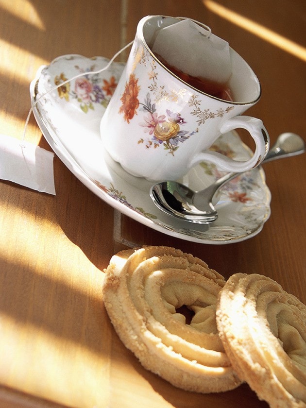 A angled close-up of a tea cup, saucer, spoon, and cookies
