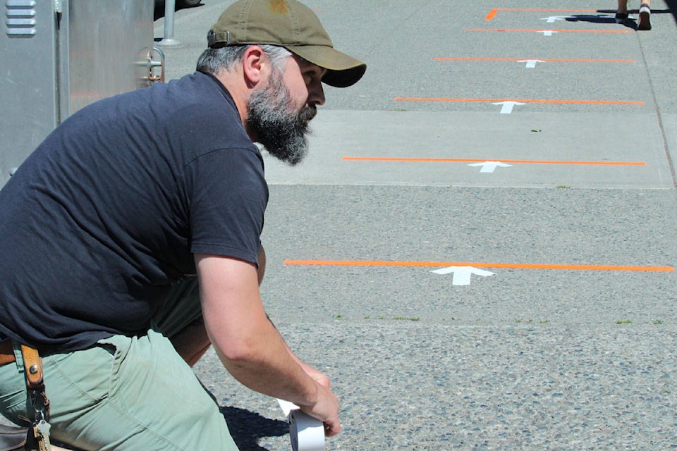 Logan Gray, owner of Discovery Coffee, tapes lines and arrows on the sidewalk outside of the Blanshard Street location. The store is set to open on May 20. (Shalu Mehta/News Staff)