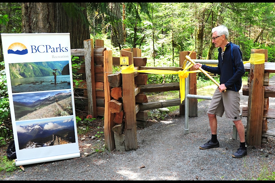 Arrowsmith Cycling Club vice-president Roy Kregosky uses a golden pickaxe to cut the ribbon of the new cycling trail at the Englishman River Falls Provincial Park on June 18, 2020. (Michael Briones photo)