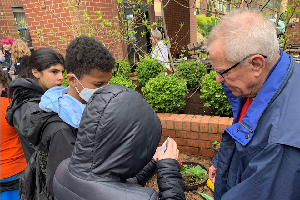 Parkwood Place resident Chuck Naylor helps Lansdowne Middle School students plant seeds in the community garden prior to making bee bombs. (Megan Atkins-Baker/News Staff)
