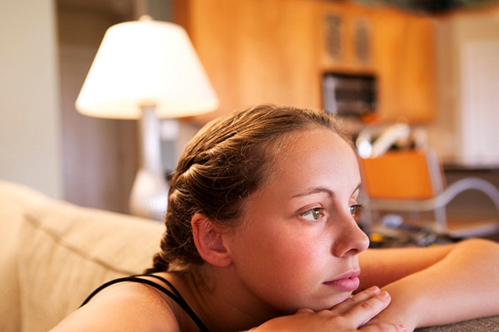 Side view of a teen girl leaning on the side of the couch and staring off into the distance