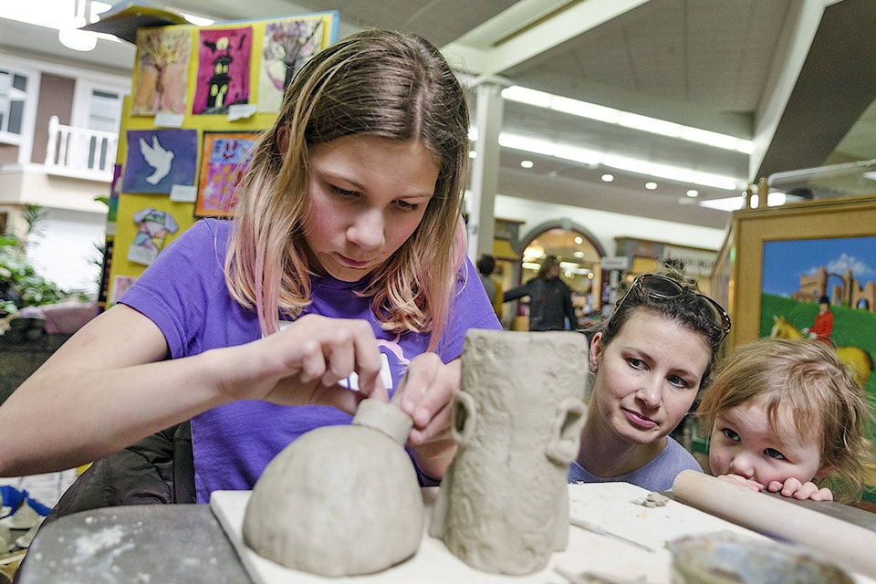 Bastion Elementary student Delilah Pieper works on the roof of her fairy house under close supervision of mom Stacey and sister Olive at the pottery workshop, part of the School District #83 Art Fair at the Mall at Piccadilly on Wednesday, March 7. (Lachlan Labere/Salmon Arm Observer)