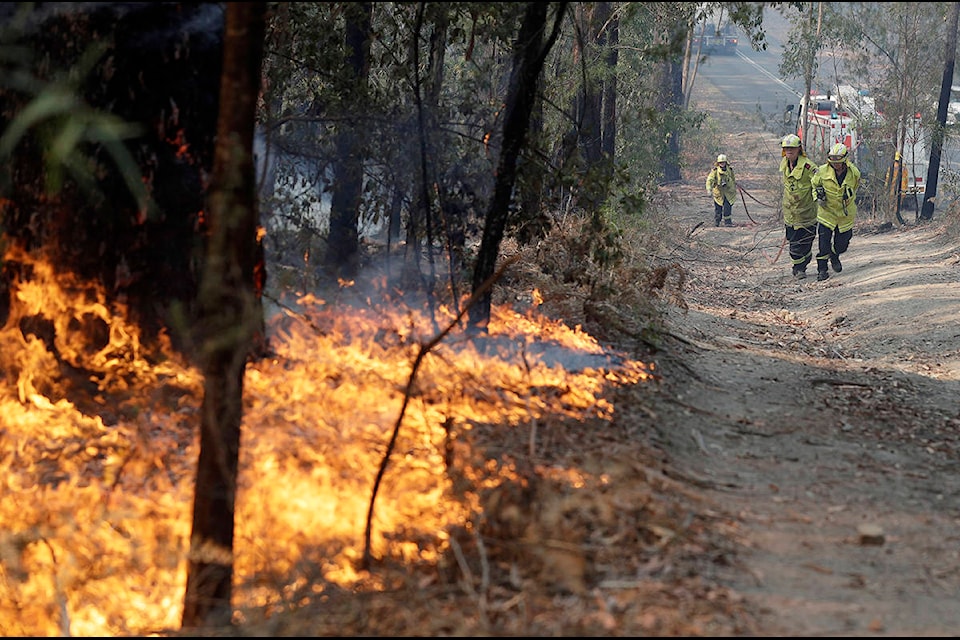 Firefighters drag a hose to battle a fire near Bendalong, Australia, Friday, Jan. 3, 2020. Navy ships plucked hundreds of people from beaches and tens of thousands were urged to flee before hot, windy weather worsens Australia’s devastating wildfires. (AP Photo/Rick Rycroft)
