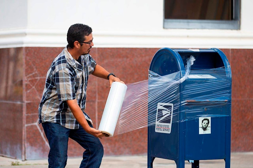 A United State Postal Service Employee covers a mailbox with plastic wrap after removing the last mail from it as the island prepares for possible impact from Hurricane Laura, Tuesday, Aug. 25, 2020, in Galveston. The plastic wrap will signals that the final mail has been cleared from the box and prevents people from placing more mail inside in case of flooding. (Mark Mulligan/Houston Chronicle via AP)