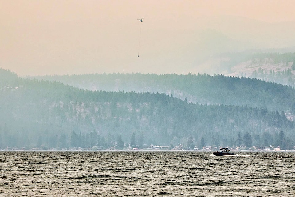 A boat cruises Okanagan Lake while a helicopter buckets the White Rock Lake wildfire burning on the Westside Aug. 11. (Darren Wolf photo)