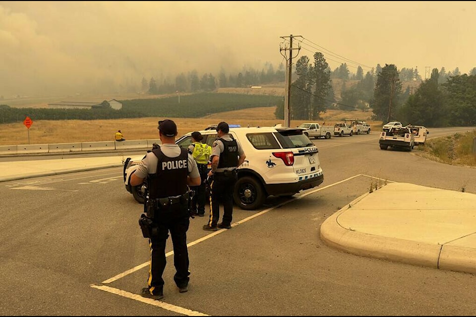 Police officers watch smoke billowing smoke from nearby wildfire at checkpoint (B.C. RCMP)