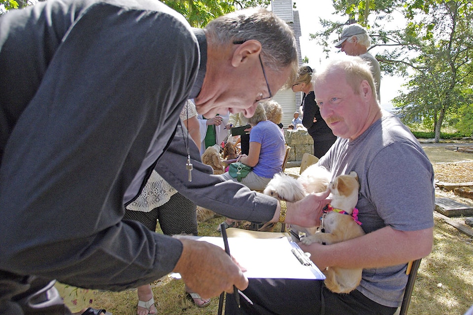 The Rev. Dr. Brett Cane from Saanichton performs a blessing for a pair of pups during Sunday’s Blessing of the Animals. (Steven Heywood/News staff)