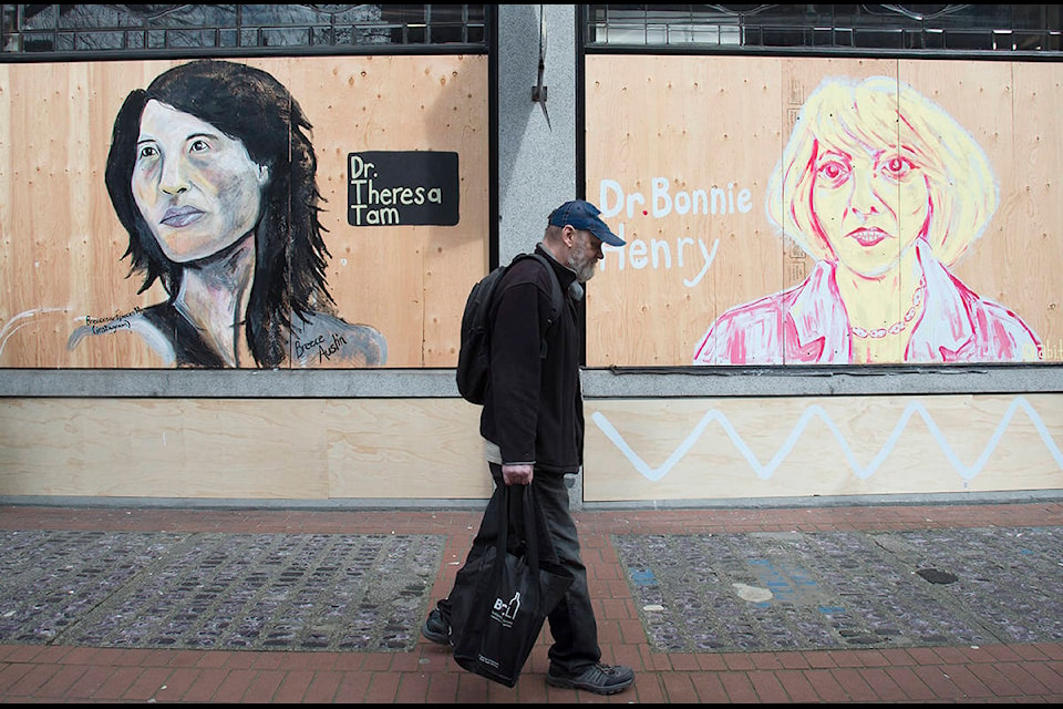 A man walks past portraits of Dr. Theresa Tam and Dr. Bonnie Henry on a boarded up business in downtown Vancouver, B.C. Wednesday, April 1, 2020. THE CANADIAN PRESS/Jonathan Hayward