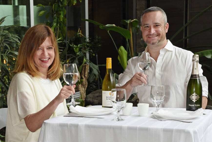 Karin Kallio from Mark Anthony Wine and Spirits, and Aidan Henry of Brink Events raise a glass to toast the return of the annual pop-up all-white picnic and dance party Diner en Blanc, which returns June 23. (Don Denton/Black Press Media)