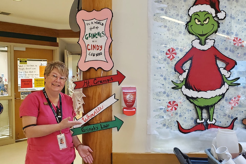 Deni House RN Fay Breck stands with some festive signage she created for the staff and residents to enjoy this holiday season. 