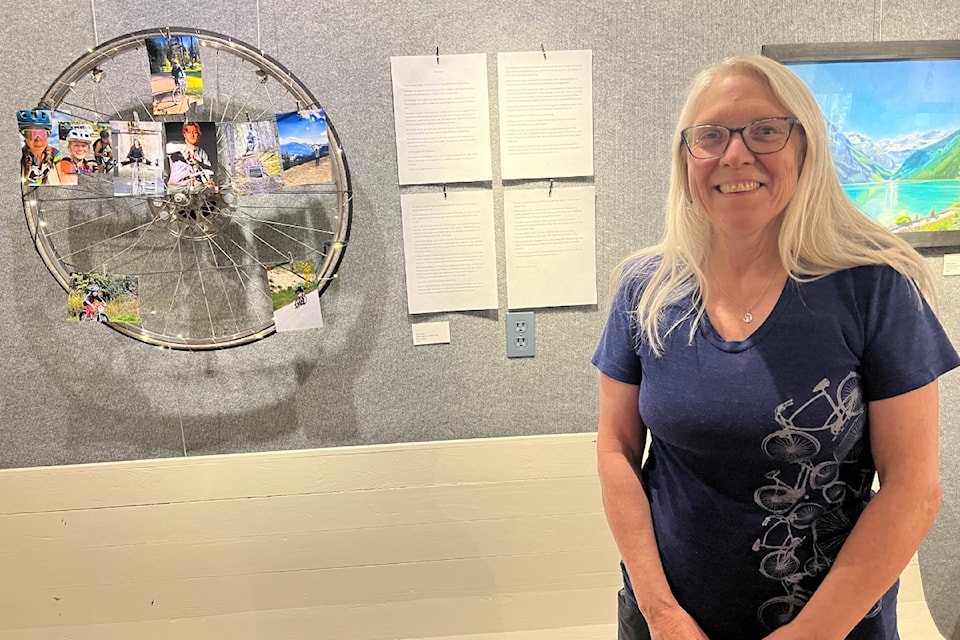 Monica Lamb-Yorski stands next to her piece in the Freedom in Motion - Bike Joy art show which integrates storytelling, photos and a bicycle wheel.