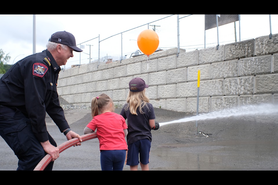 Captain Don Firth helps siblings Emilia and Reid work together to put out 'fires' at the Williams Lake Fire Department's annual open house. 
