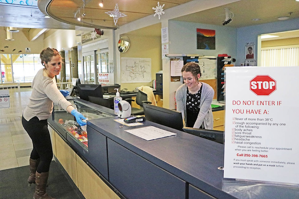 Natalie Swift and Bailey Schick, cashier clerks for the Cariboo Memorial Recreation Complex, take the time to wipe down and disinfect their workplace on Saturday, March. 14. (Patrick Davies photo - Williams Lake Tribune)