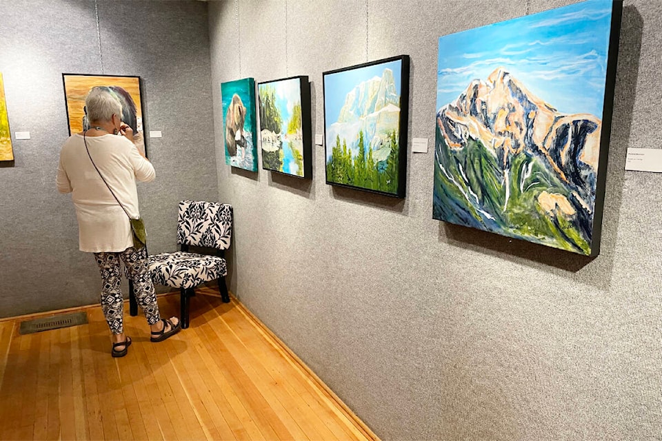 An art show opening patron views some of the paintings by Garry Toop. (Ruth Lloyd photo - Williams Lake Tribune)