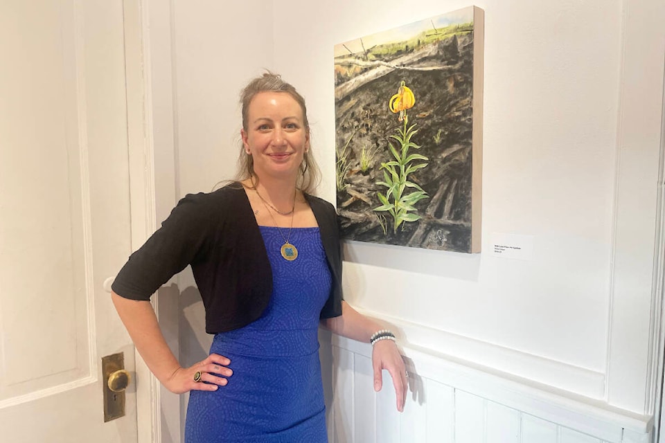 Leah Selk stands next to her piece With Love from the Cariboo, which she said sums it up, with a tiger lilly flower blooming in the midst of a burned landscape. The piece is part of her show now on display in the upper gallery of the Station House Gallery. (Ruth Lloyd photo - Williams Lake Tribune)