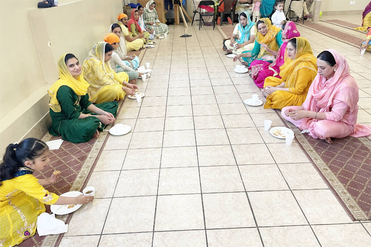 Community members sit on the floor on carpets and eat during Vaisakhi celebrations at Gurdwara Sahib Western Singh Sabha Association on May 13, 2023. (Ruth Lloyd photo Efteen)