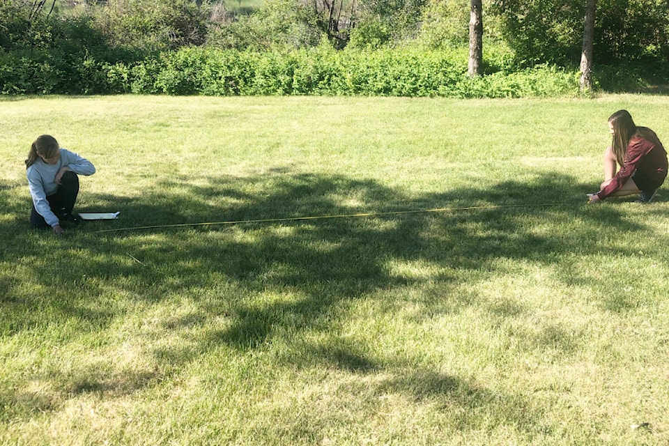 Alaina Dyck and Alyna Obexer measure a tree’s shadow. Students were able to put their math skills into practice using them at Scout Island to calculate the height of trees. (Photo submitted)