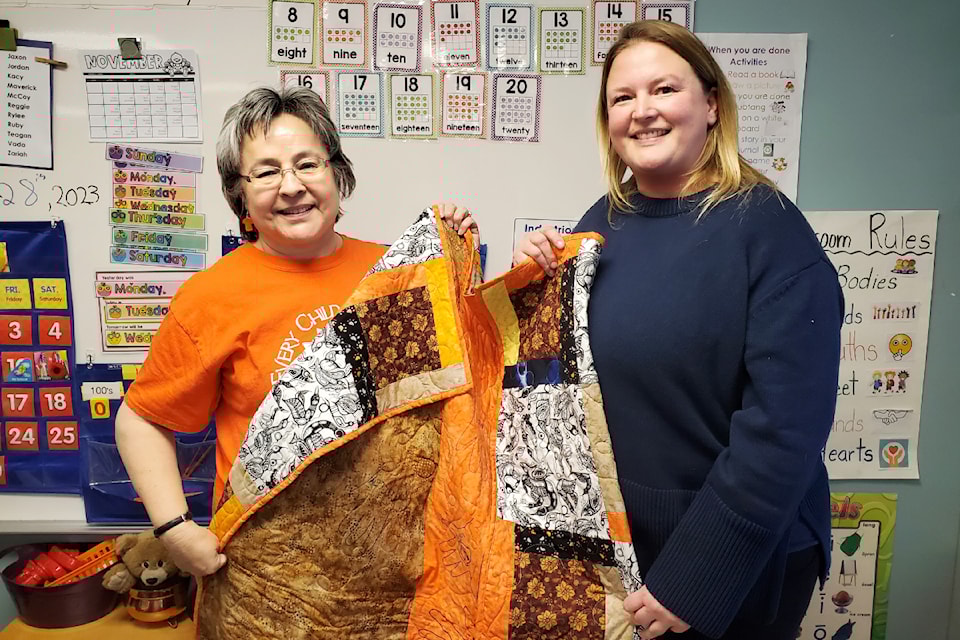 Phyllis Webstad, left, and teacher Karyn Sache show how one side of the quilt for a residential school survivor features the hand prints from students at Cataline Elementary School who helped create the quilt in fall of 2023. 