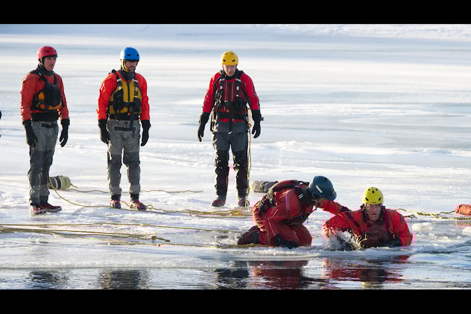 One of the water rescue trainees lunges back through a hole cut near the edge of the frozen surface of the Yukon River in downtown Whitehorse on Jan. 8, 2025. (Jim Elliot/Yukon News)