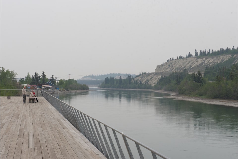 Onlookers look through the smoke-induced haze at the Yukon River in downtown Whitehorse on June 13, 2025 (Talar Stockton/Yukon News) 