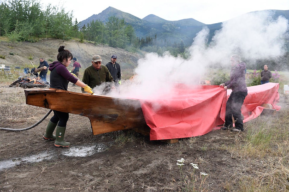 Carving apprentice Violet Gatensby, left, uses a hose connected to a creek to add water to a dugout canoe on July 20 on the grounds of the old Chooutla School in Carcross as master master Wayne Price, to her right, watches. Price and Gatensby had spent 63 days carving the canoe out of a cedar trunk and were in the process of stretching it, using steam to make the wood more malleable. (Jackie Hong/Yukon News)