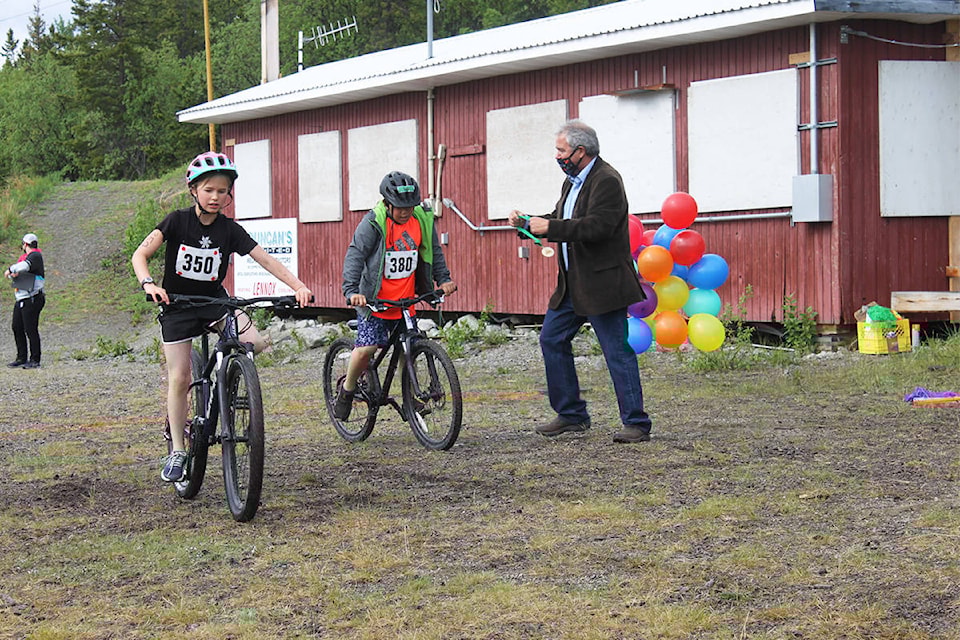 Two participants cross the finish line at the City of Whitehorse Kids Triathlon on June 12 with Mayor Dan Curtis on hand to present medals. (Stephanie Waddell/Yukon News)
