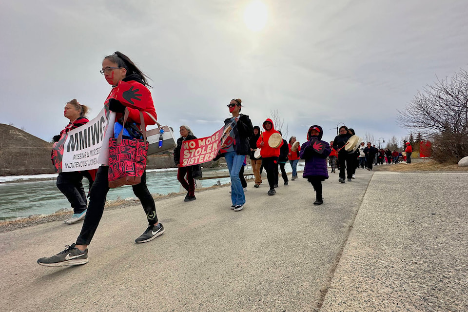 The march proceeds quietly along the riverfront, with participants banging drums, wearing red and carrying signs. (Gabrielle Plonka/Yukon News)